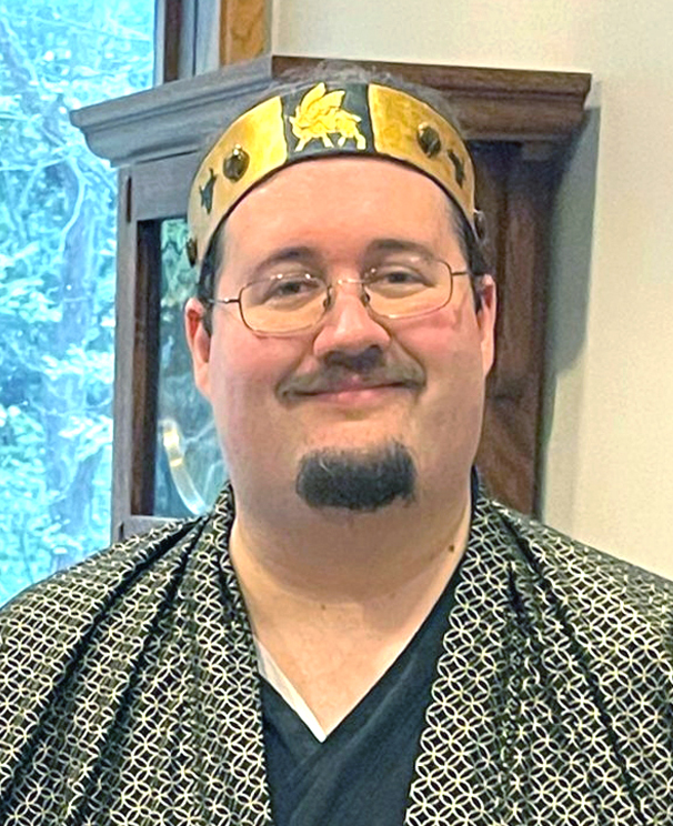 Baron wearing a patterned coat, wearing a gold coronet, smiling at the camera