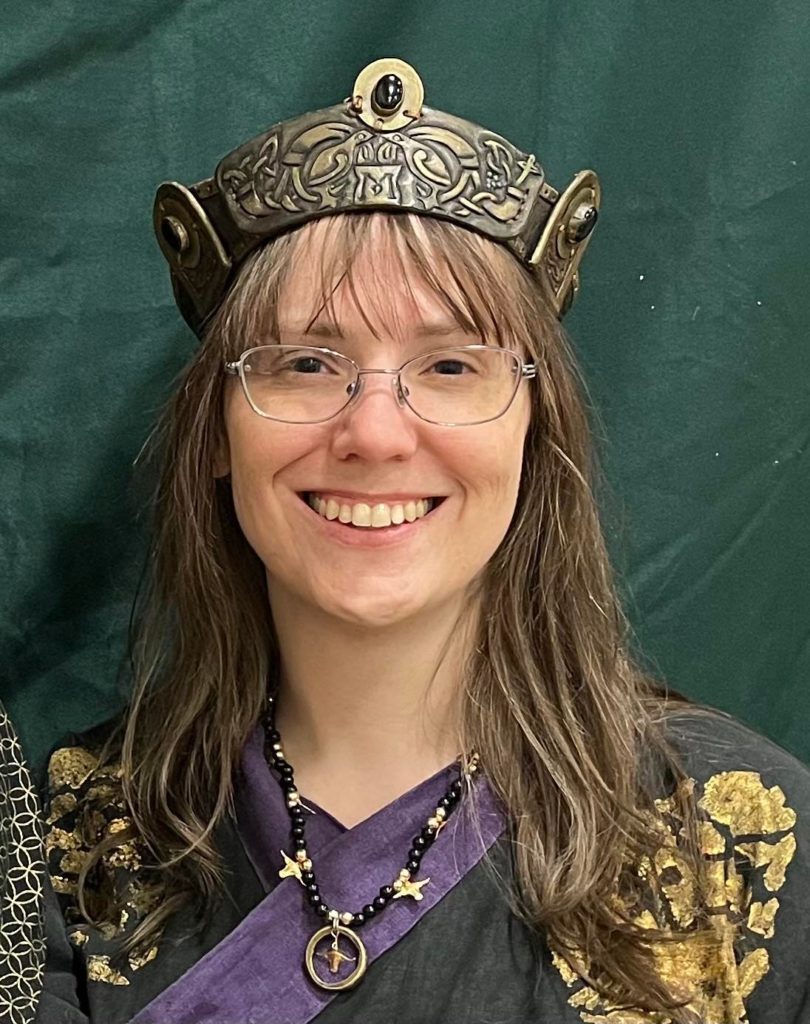 Baroness in a black, gold, and purple dress, wearing a coronet, smiling at the camera
