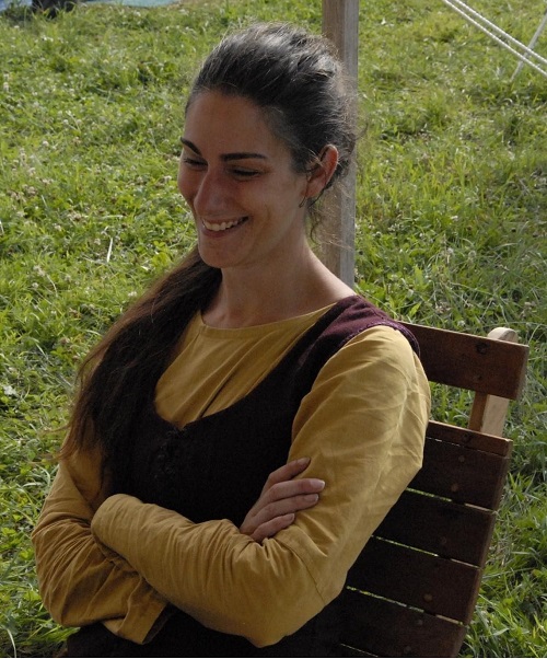 A woman sitting in a wooden chair wearing a yellow underdress and dark overdress