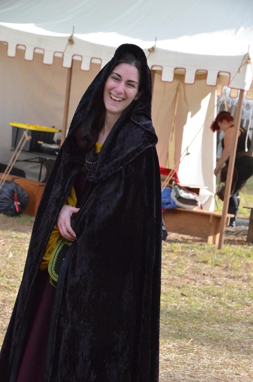 A woman standing in front of a canvas tent, wearing a long black cloak
